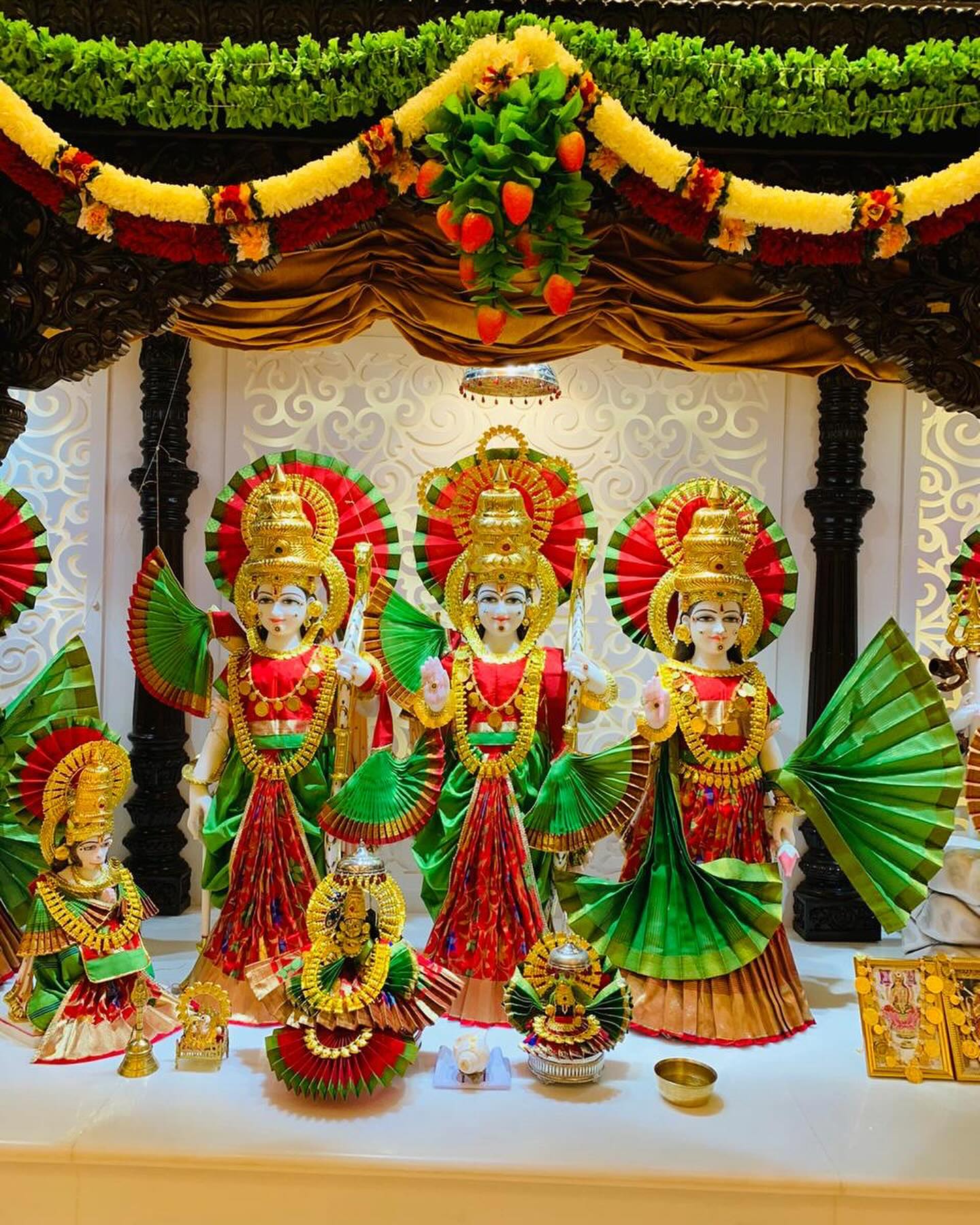 Group of deities presented in coordinated red, green and gold poshak and shringar.