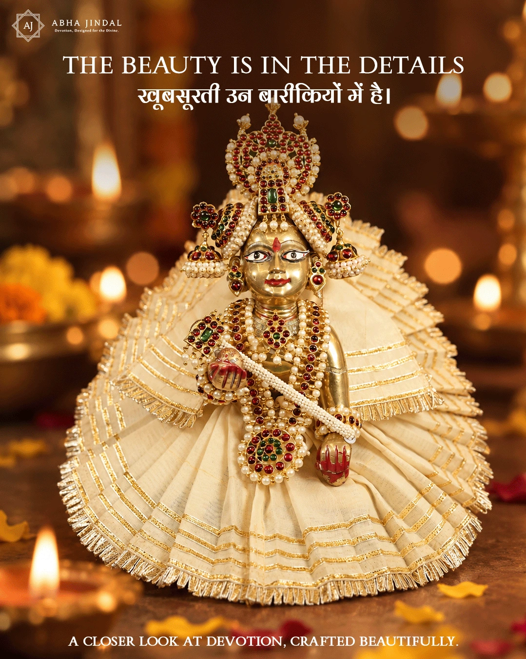 Front view of Laddu Gopal Ji in a pleated cream poshak with gold-tone bands and fringe, red and green floral shringar, a tall rounded mukut and pale bead-like accents.