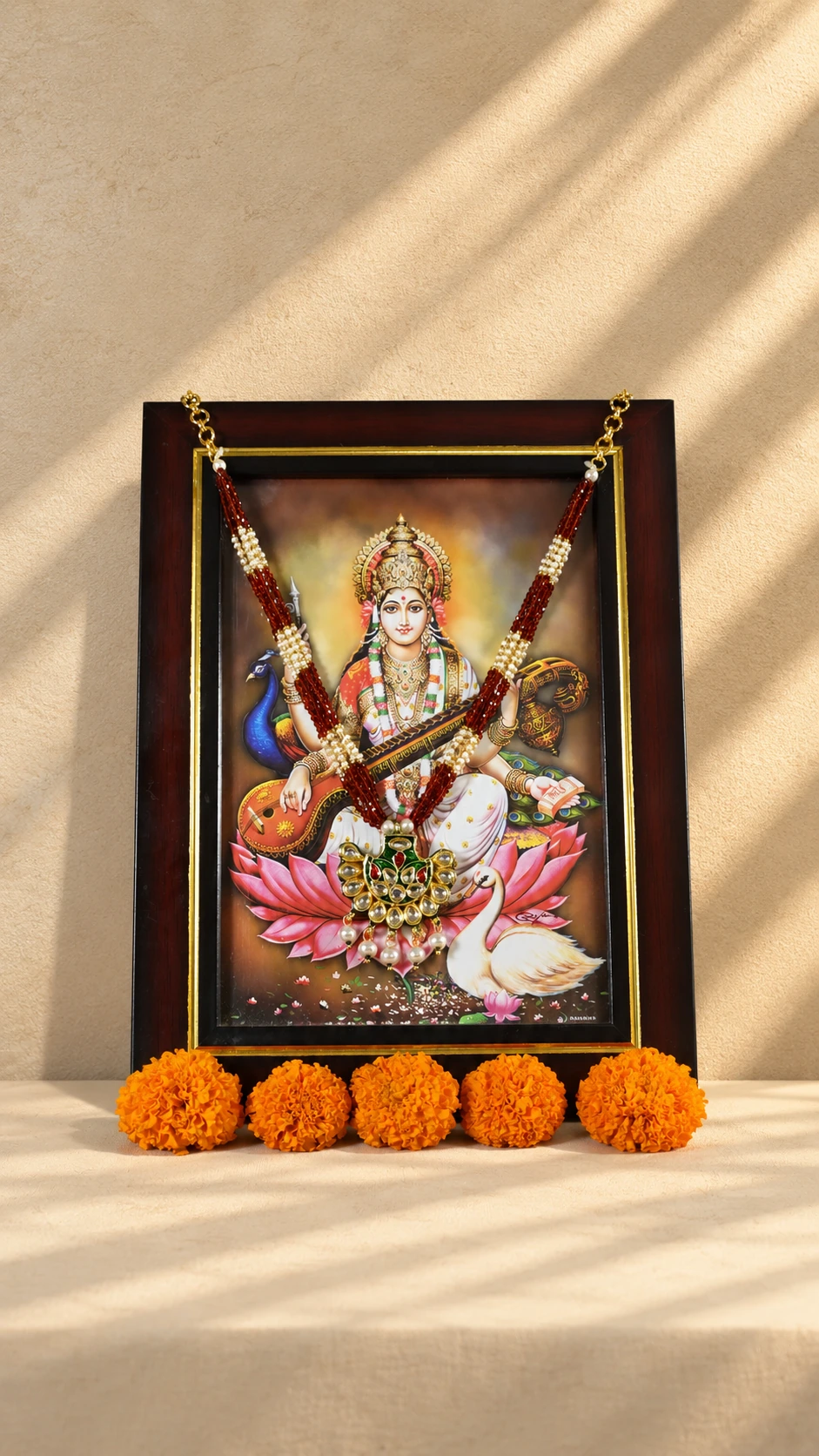 Deep red bead photo mala with ivory-coloured bands and a floral pendant, shown on a framed Saraswati Ji photograph.