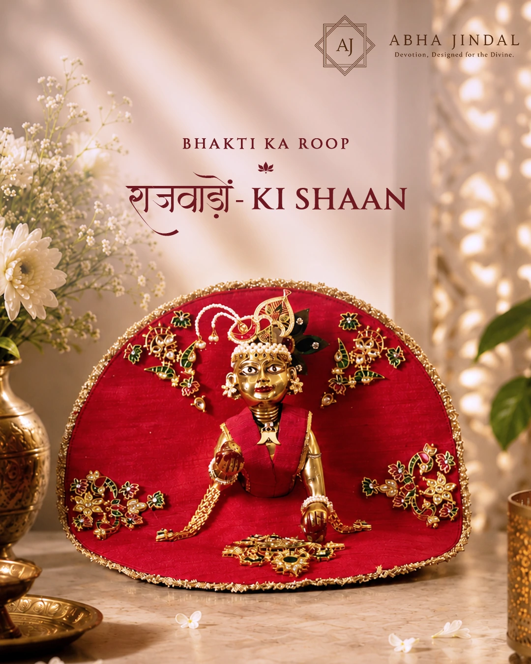 Laddu Gopal in a red fan-shaped Rajwada poshak with floral ornaments and a gold-tone border.