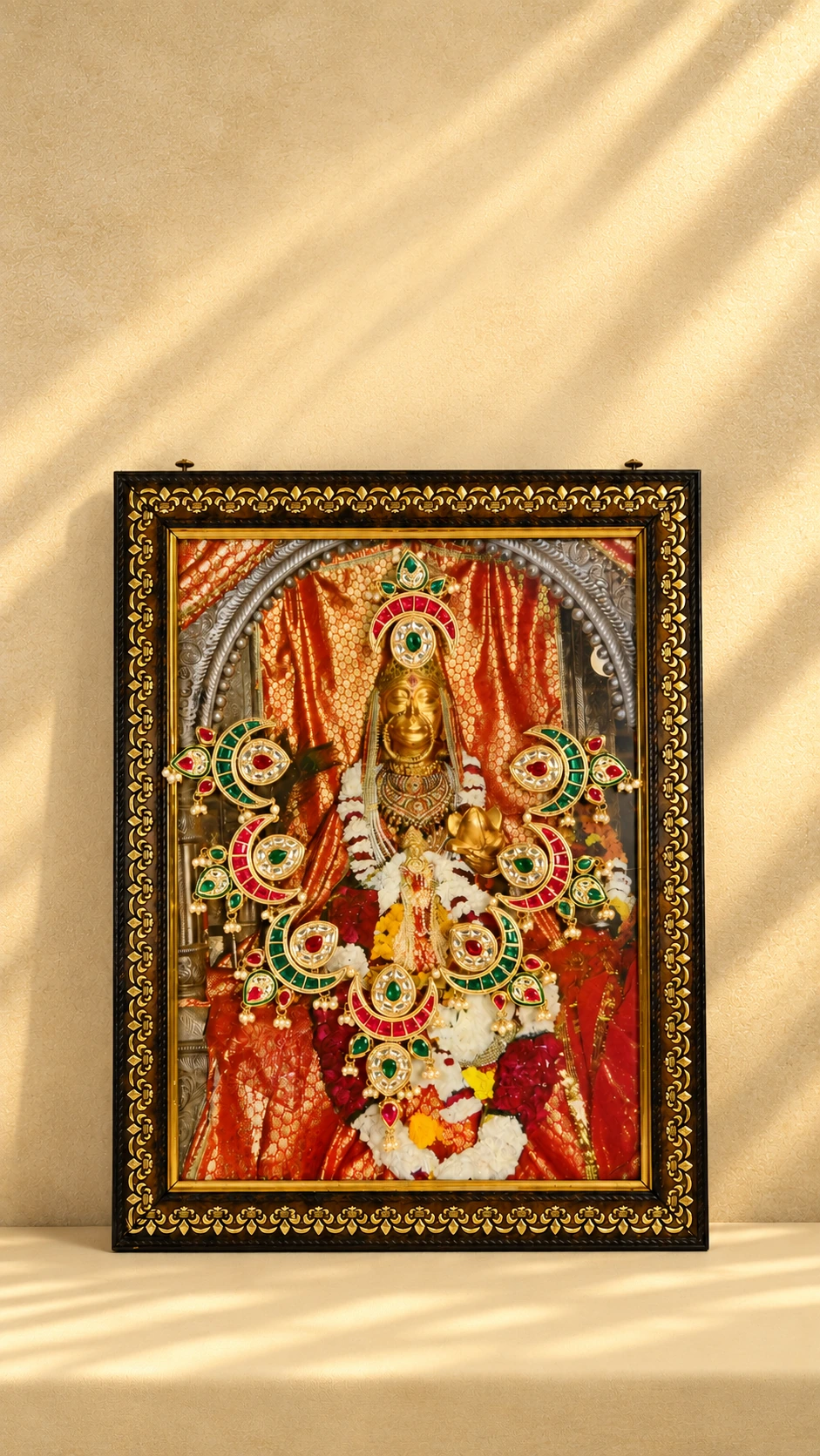 Red and green crescent photo mala with decorative drops, displayed across a framed devotional photograph.