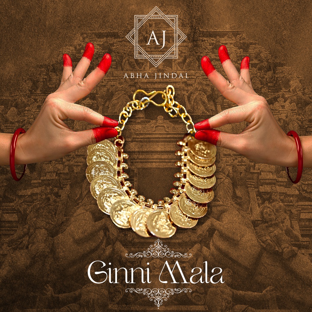 Coin-style gold-tone mala held in a circle between two hands against a brown backdrop