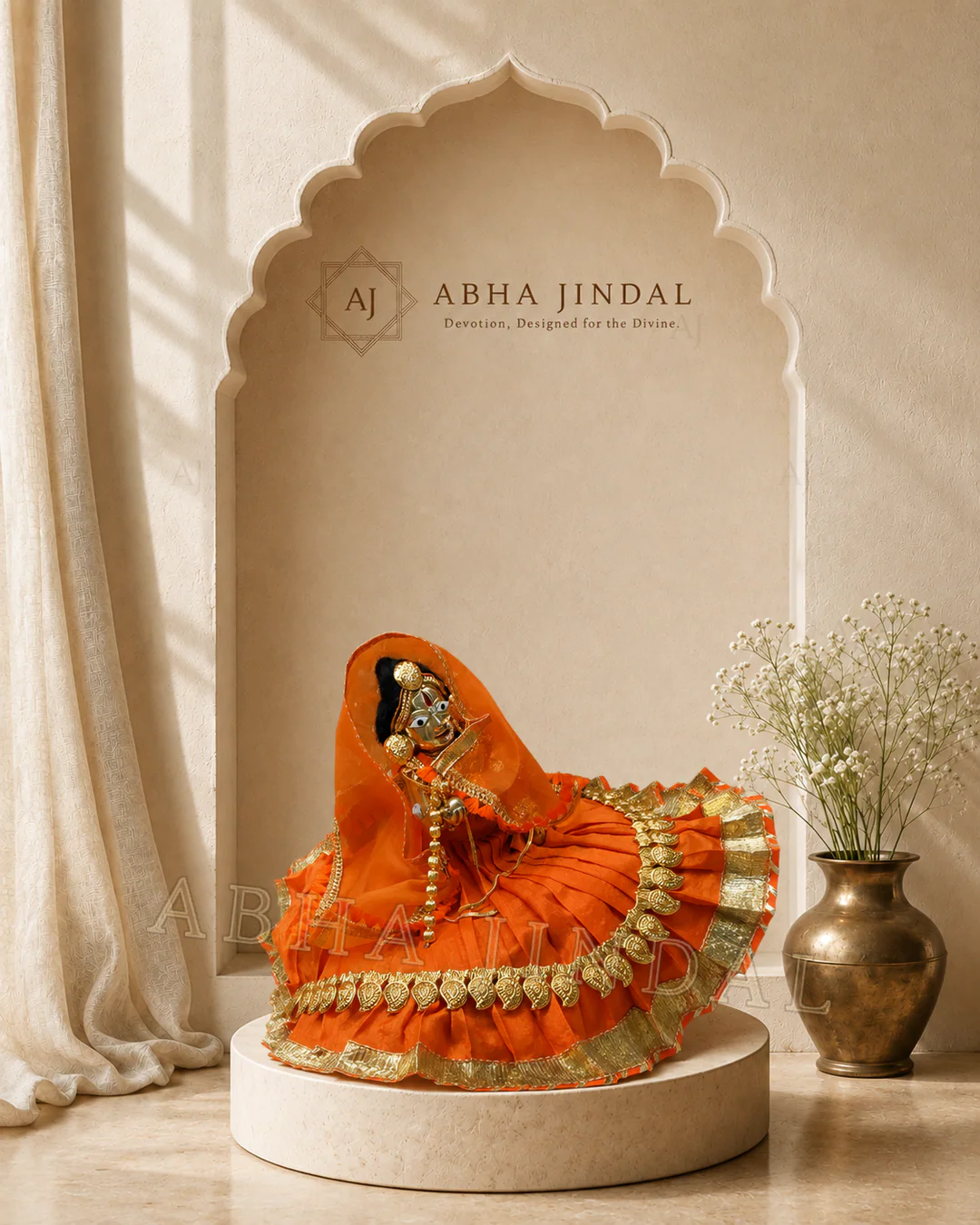 Front view of Laddu Gopal in a saffron-orange veil and pleated skirt with round gold-tone accents