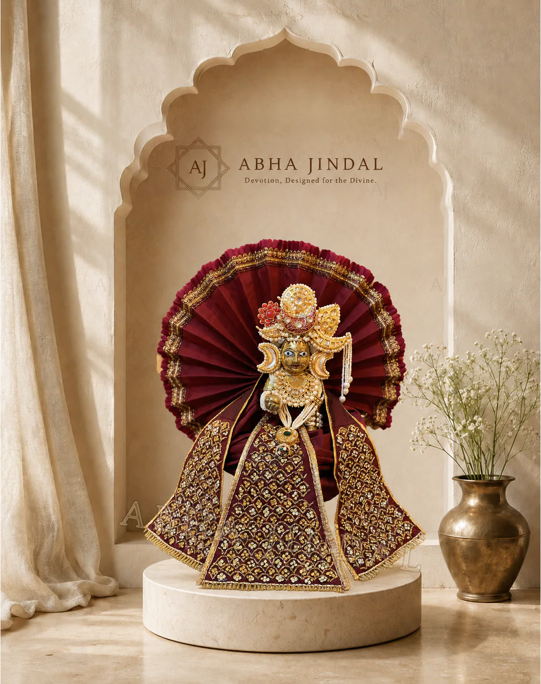 Laddu Gopal in beige and maroon attire before a tall fan-shaped maroon backdrop