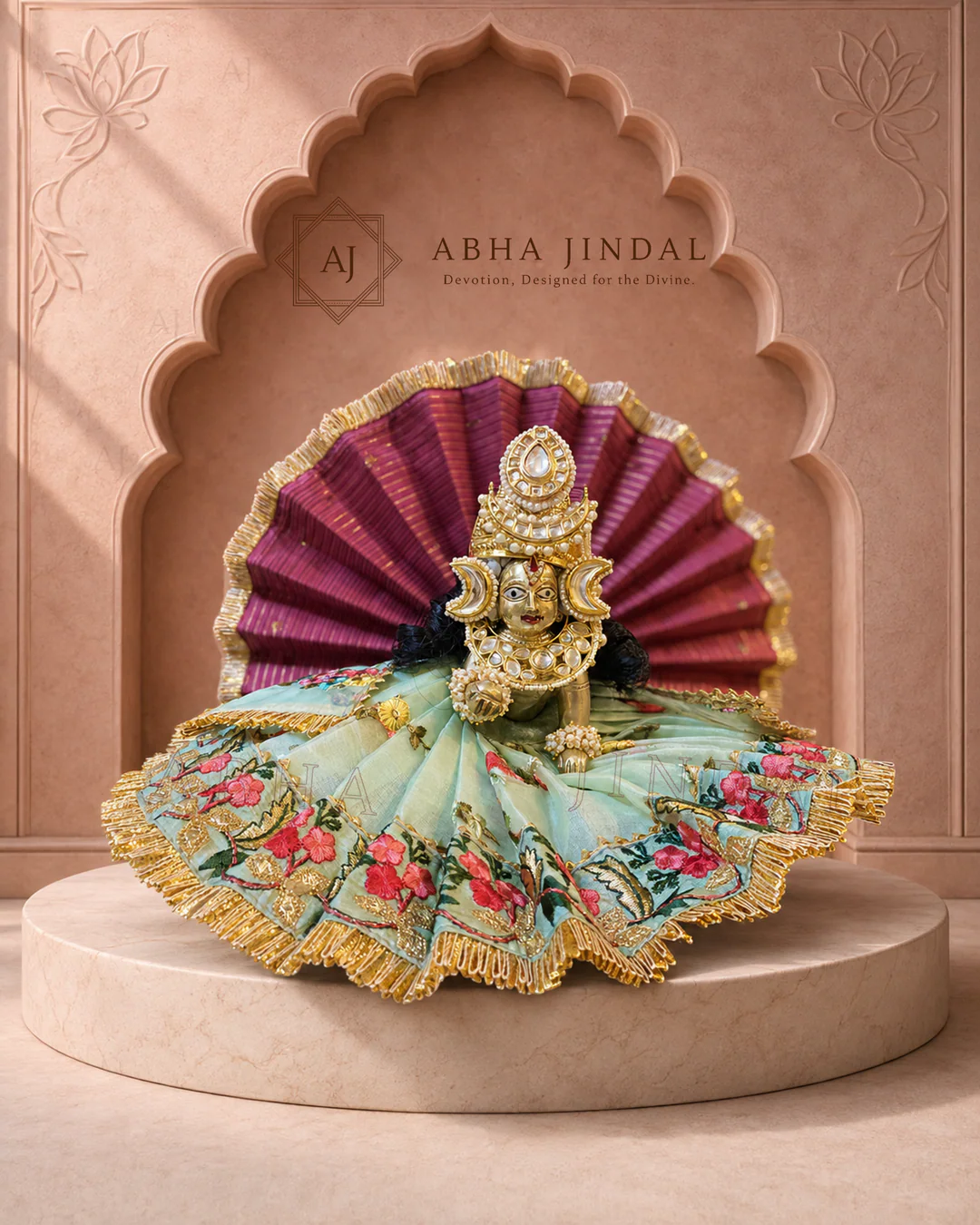 Laddu Gopal in sage-blue floral attire with gold-tone edging and a maroon fan surround