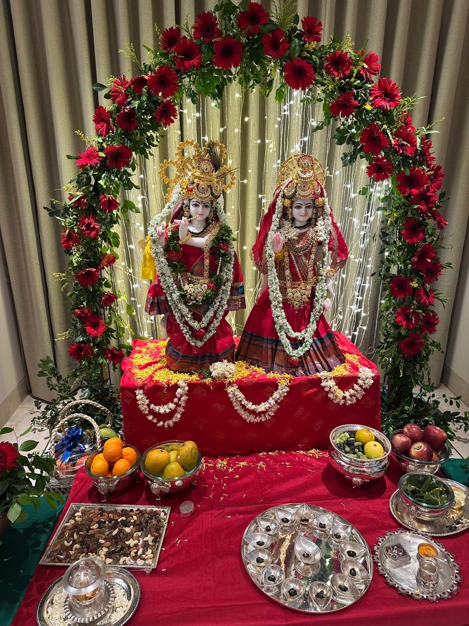 Two richly dressed ceremonial figures with jewellery, flowers, fruit and ritual plates.