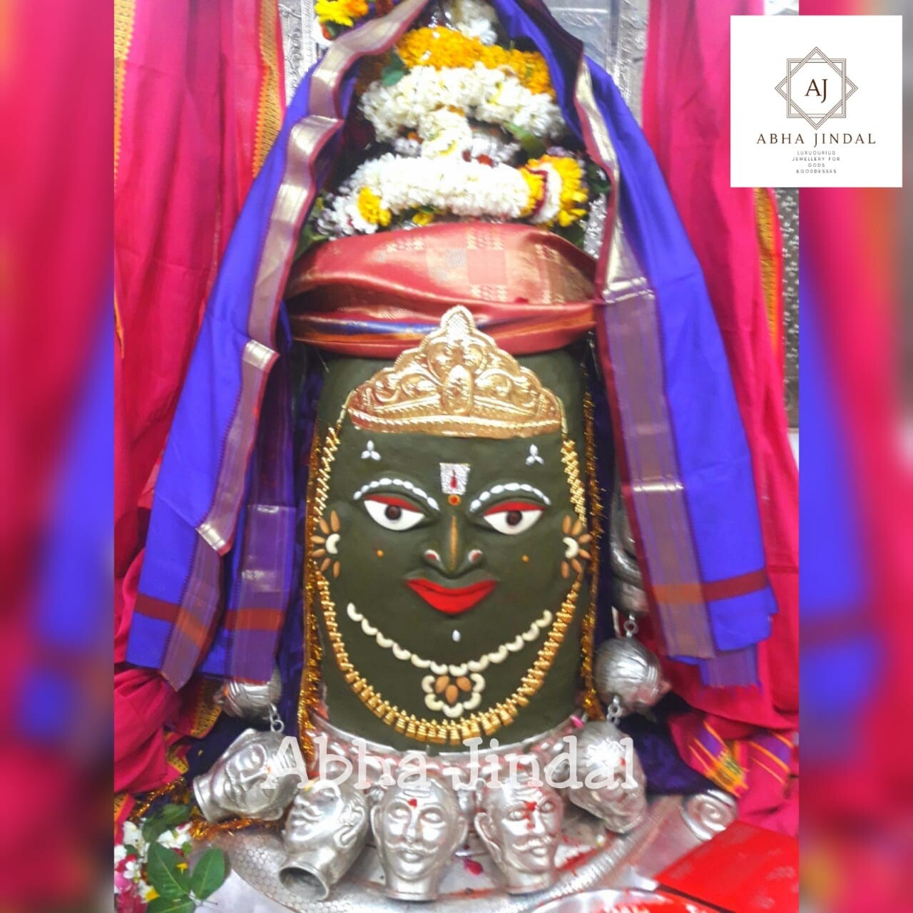 Close view of Mahakaleshwar Jyotirlinga with painted face, gold-toned crown, flower garlands, colourful drapery and silver forms.